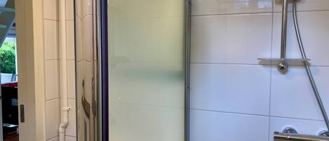 Un baño con cabina de ducha de vidrio, paredes cubiertas de azulejos blancos y encimera blanca.