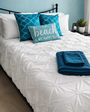 A bed with white bedding and a single blue pillow with text.