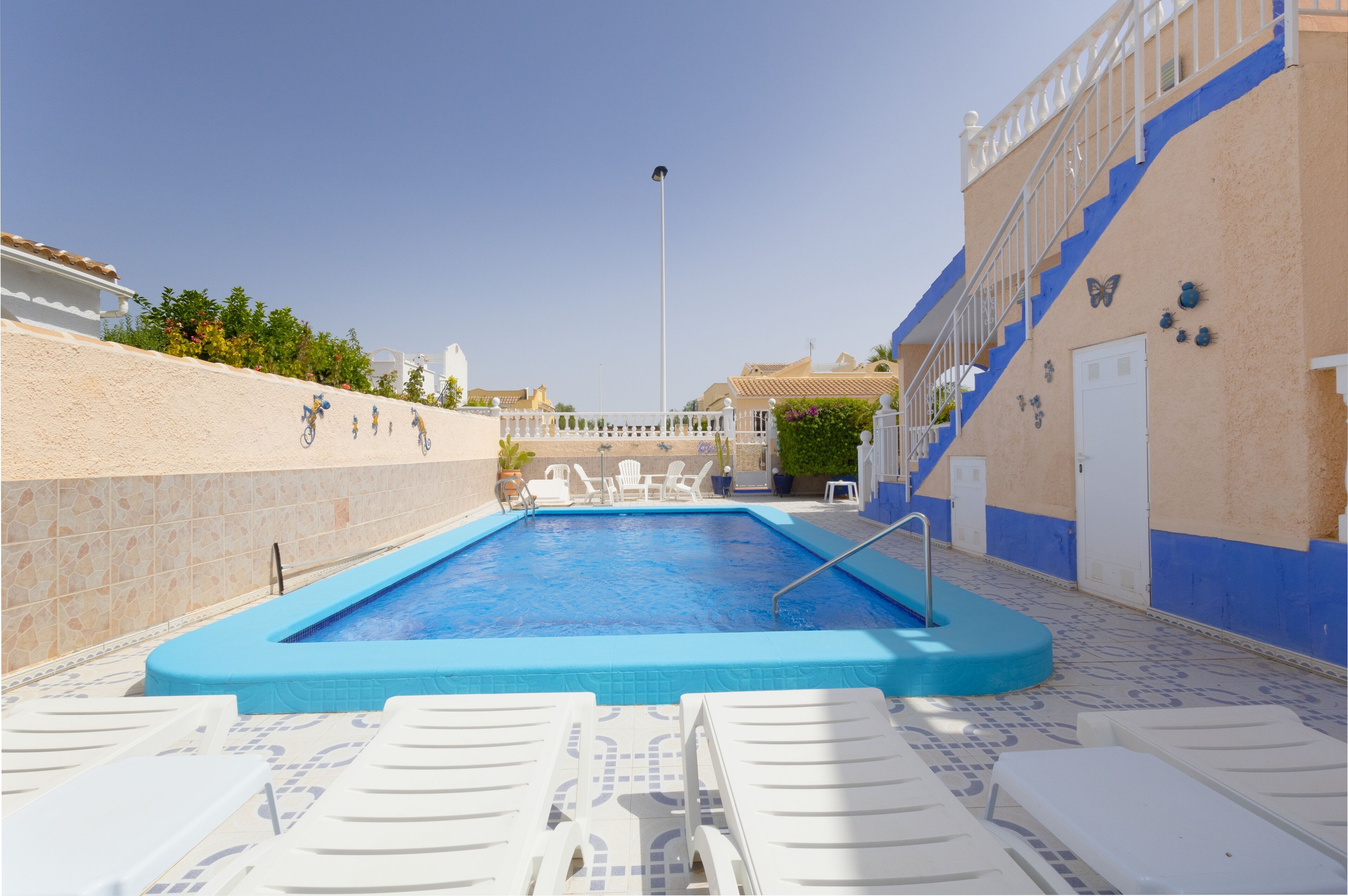 Ein Schwimmbecken mit blauen Fliesen, weißen Liegestühlen und einer Treppe mit blauen Akzenten.