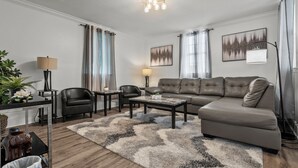 A modern living room with a sectional sofa, two armchairs, a coffee table, and a rug. There are two lamps, a plant, and artwork on the walls. - Perfect Get-Away In The Heart Of Downtown Florence (Florence)