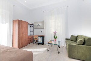 Een moderne hotelkamer met een bed, een bureau met stoel, een bank, een glazen tafel en een potplant.