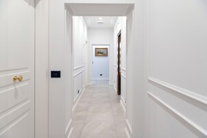 A narrow hallway with white walls and a tiled floor, leading to a door with a gold handle.