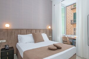 Hotellihuone, jossa on sänky, yöpöytä ja ikkuna, josta avautuu näkymä tiilitaloon.