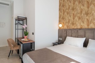 Camera d'hotel con un letto, una scrivania con una sedia, uno scaffale con una pianta e un muro con un motivo a foglia.