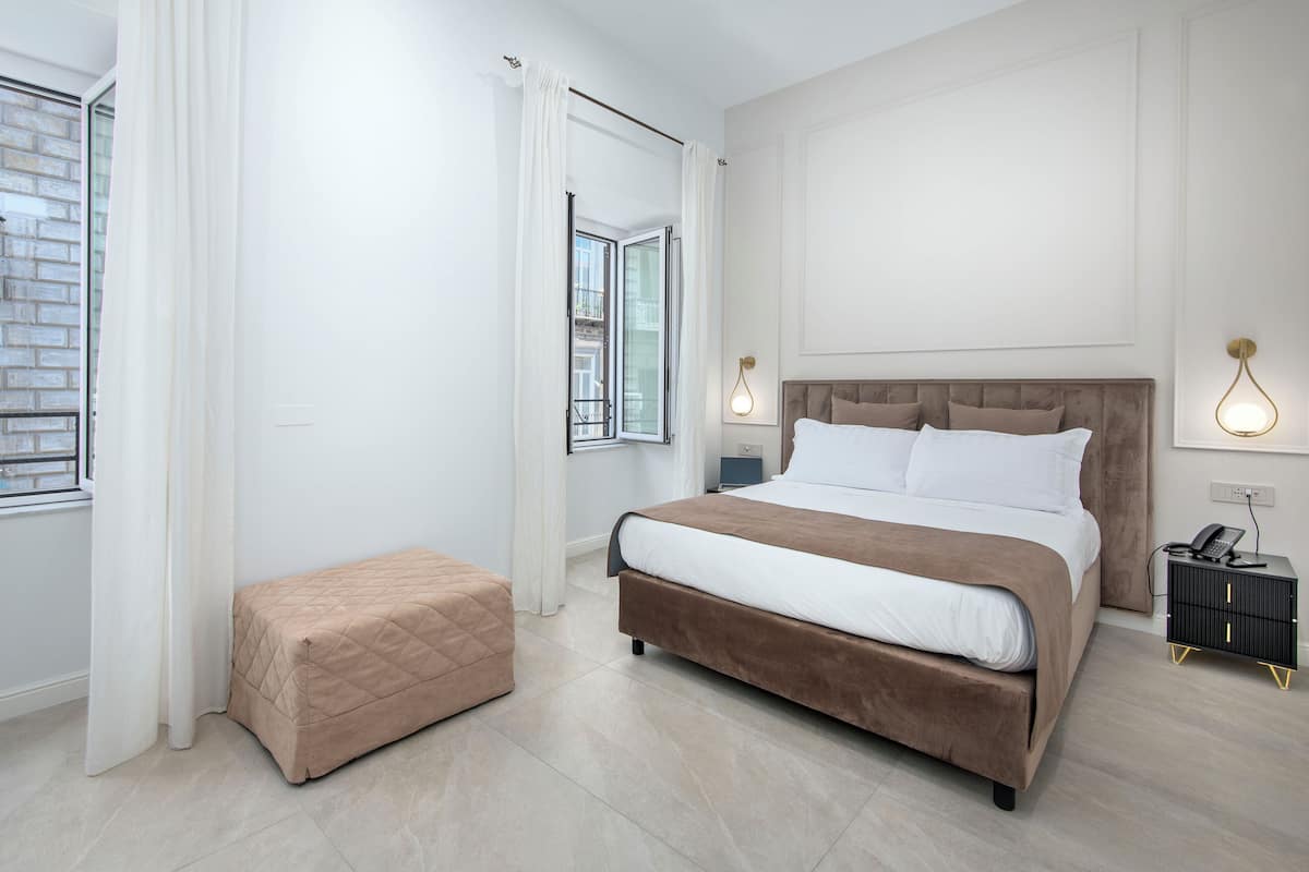 A modern bedroom with a large bed, a bedside table, a nightstand, and a window with curtains.