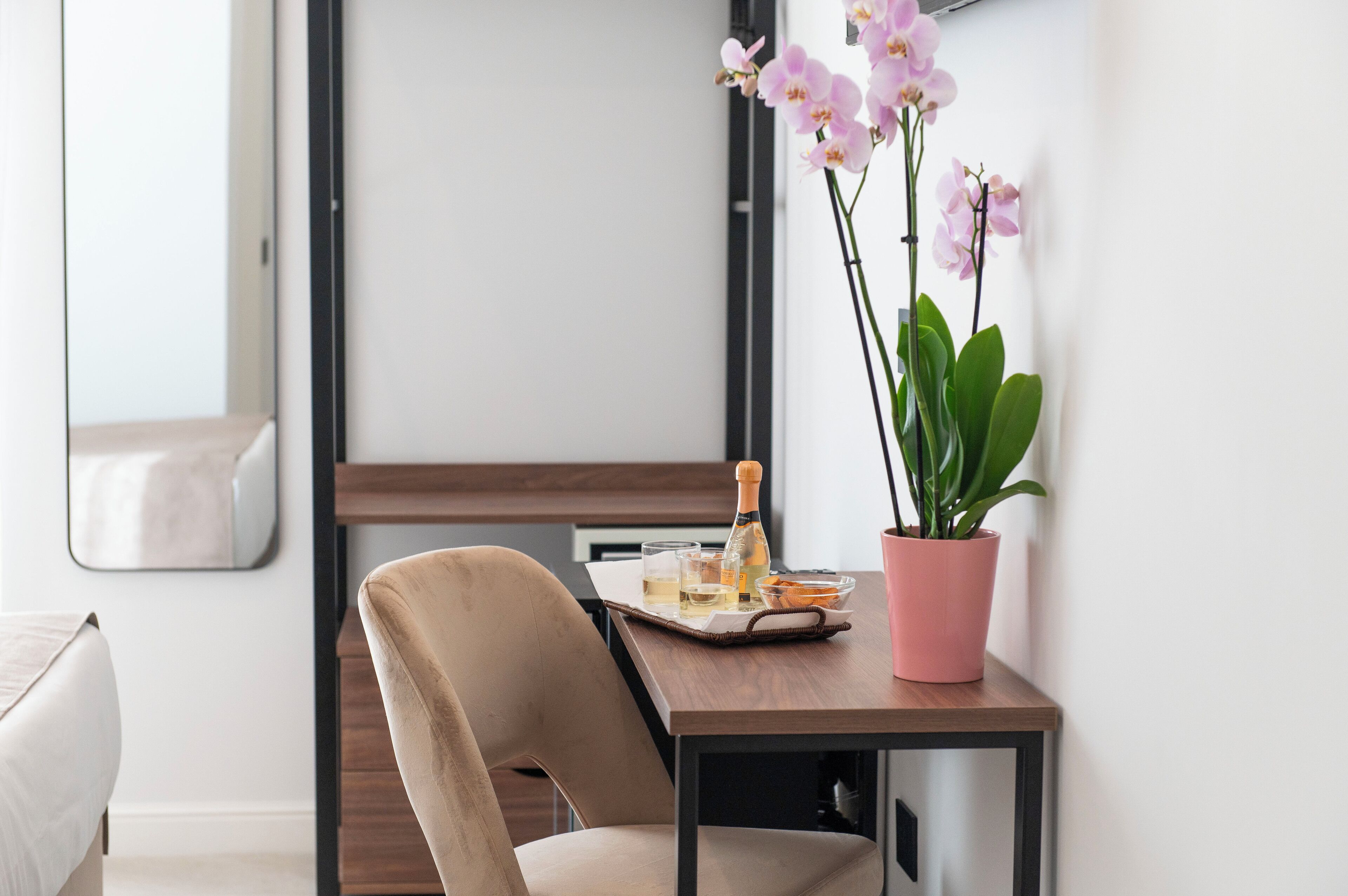A modern room with a wooden table, a chair, a potted orchid, and a bottle of champagne.