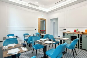 Een hotelkamer met een zithoek met blauwe stoelen en tafels, een kitchenette en een receptie.