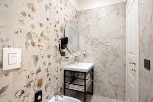 Een badkamer met een wit wastafelmeubel, een spiegel, een zwarte handdoekhouder en bloemenbehang.
