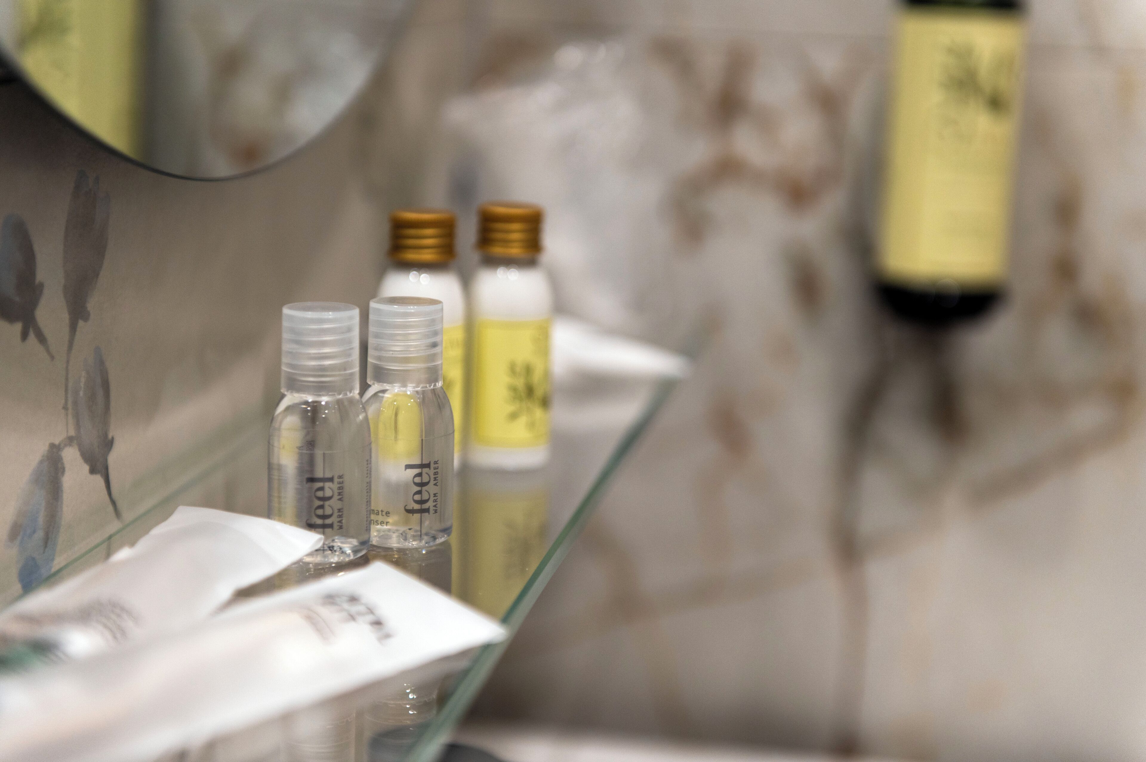 A bathroom with a glass shelf holding toiletries and a mirror reflecting the room.