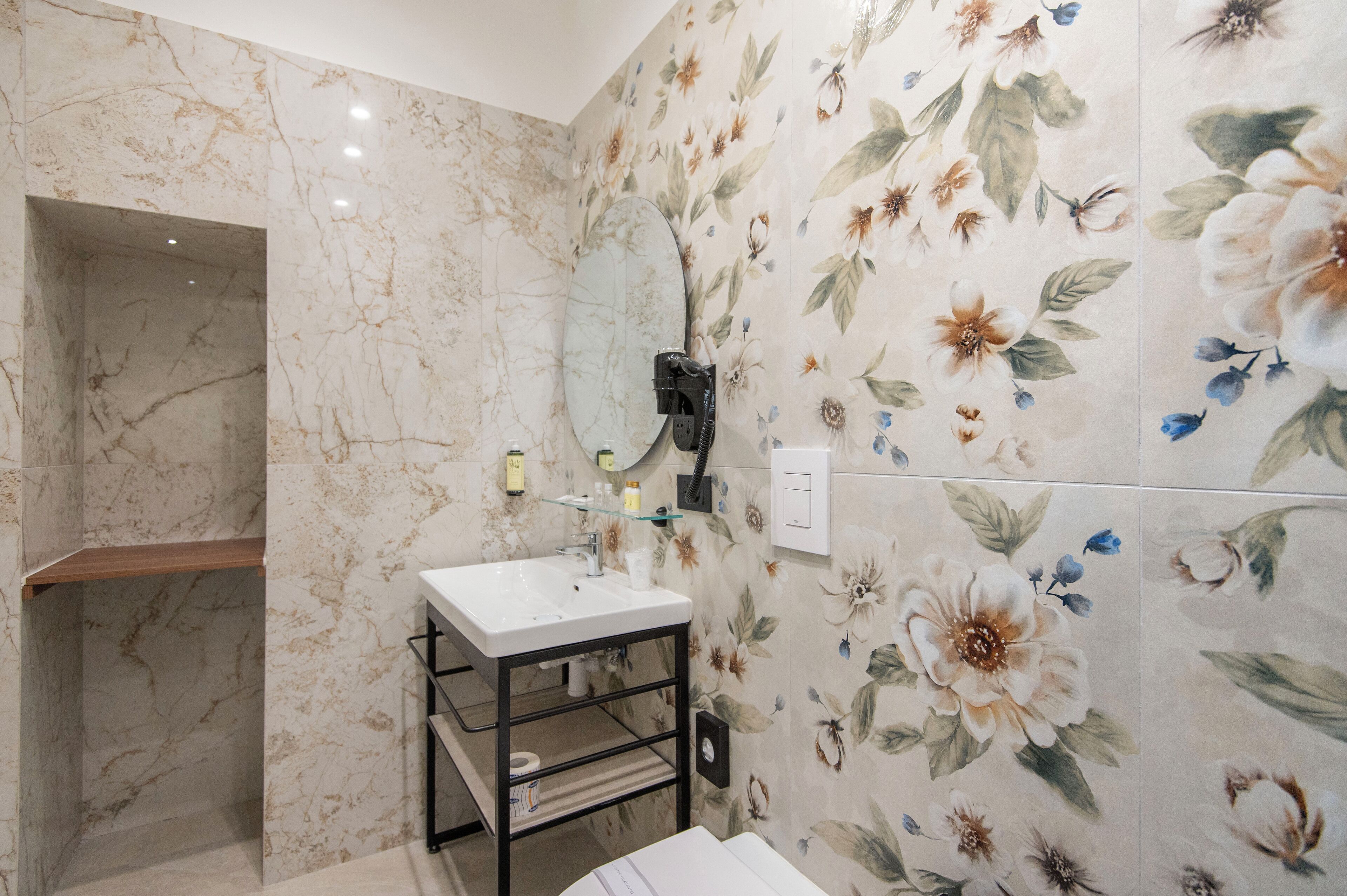 Un baño con pared de mármol, un lavabo blanco, un espejo y un papel tapiz floral.