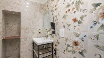 Un baño con pared de mármol, un lavabo blanco, un espejo y un papel tapiz floral.