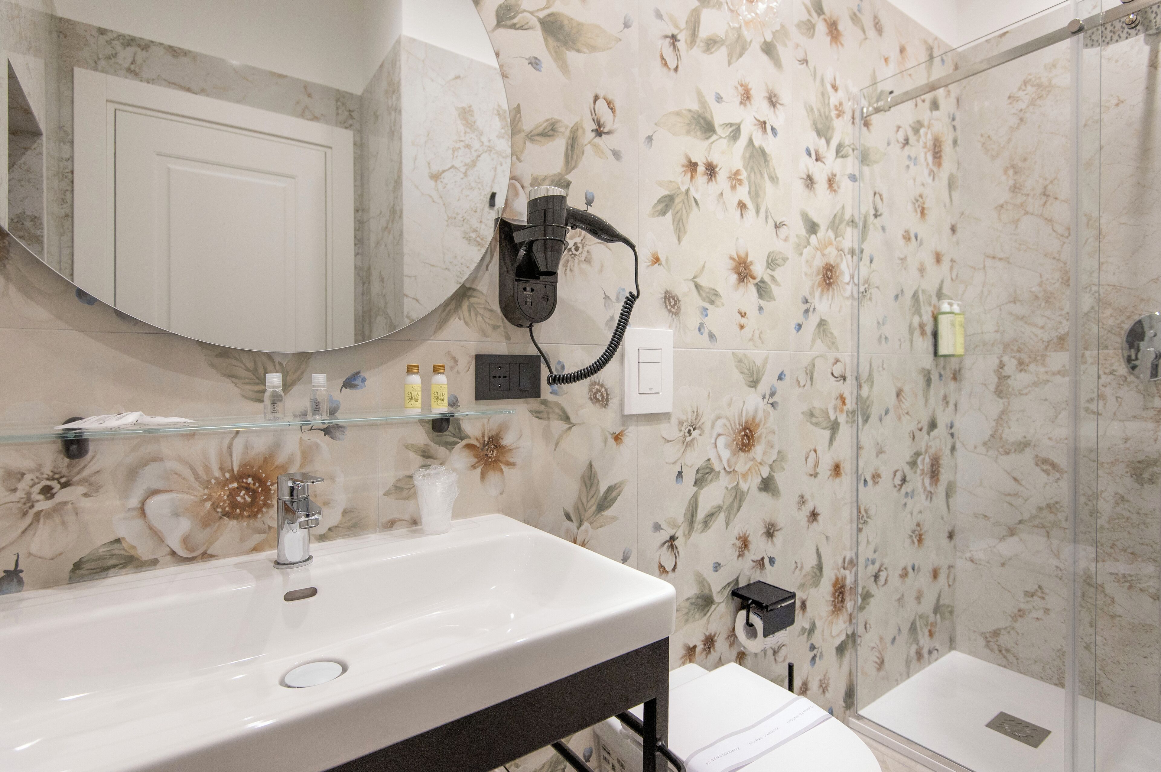 Un bagno con un ampio specchio, un lavandino, un asciugacapelli e una zona doccia.