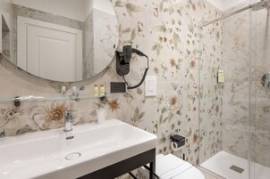 Un baño con un espejo grande, lavamanos, secador de pelo y zona de ducha.