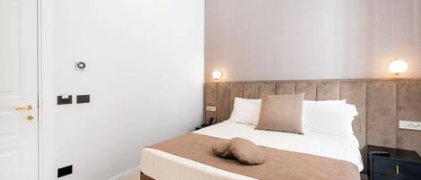 A modern hotel room with a large bed, a wooden headboard, bedside lamps, and a nightstand.
