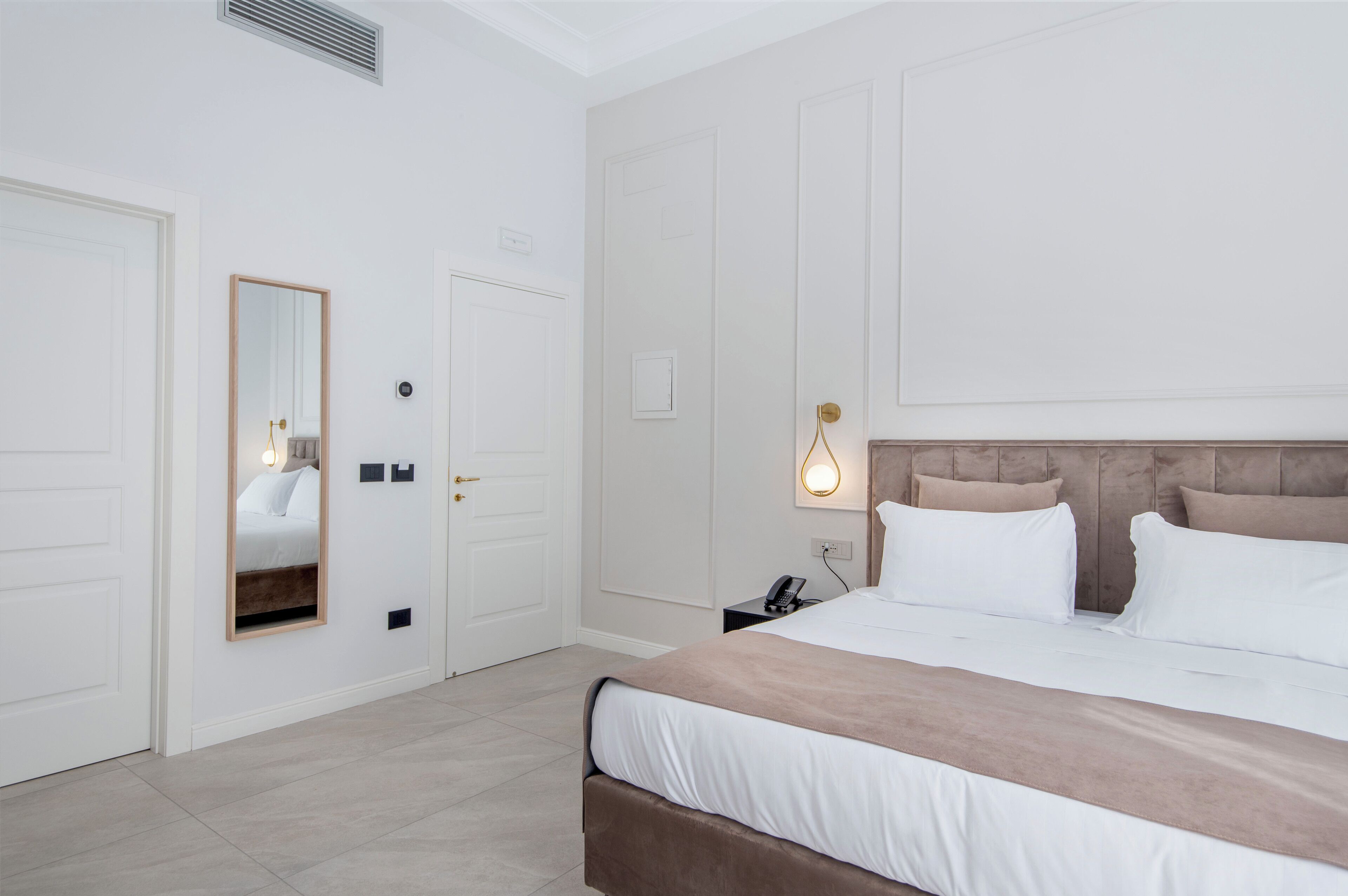 A hotel room with a large bed, a bedside table with a lamp, a mirror, and a door.