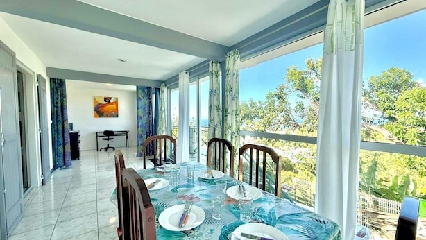 Un coin repas avec une table dressée pour quatre personnes, de grandes fenêtres et une vue sur la verdure.