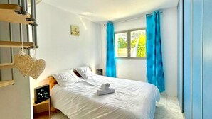 Une chambre à coucher avec un lit, une table de chevet, une fenêtre avec des rideaux et une vue sur la verdure à l’extérieur.