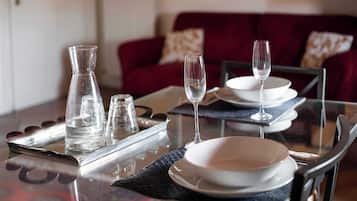 Una mesa de comedor dispuesta con platos, vasos y una jofaina, con un sofá rojo al fondo.