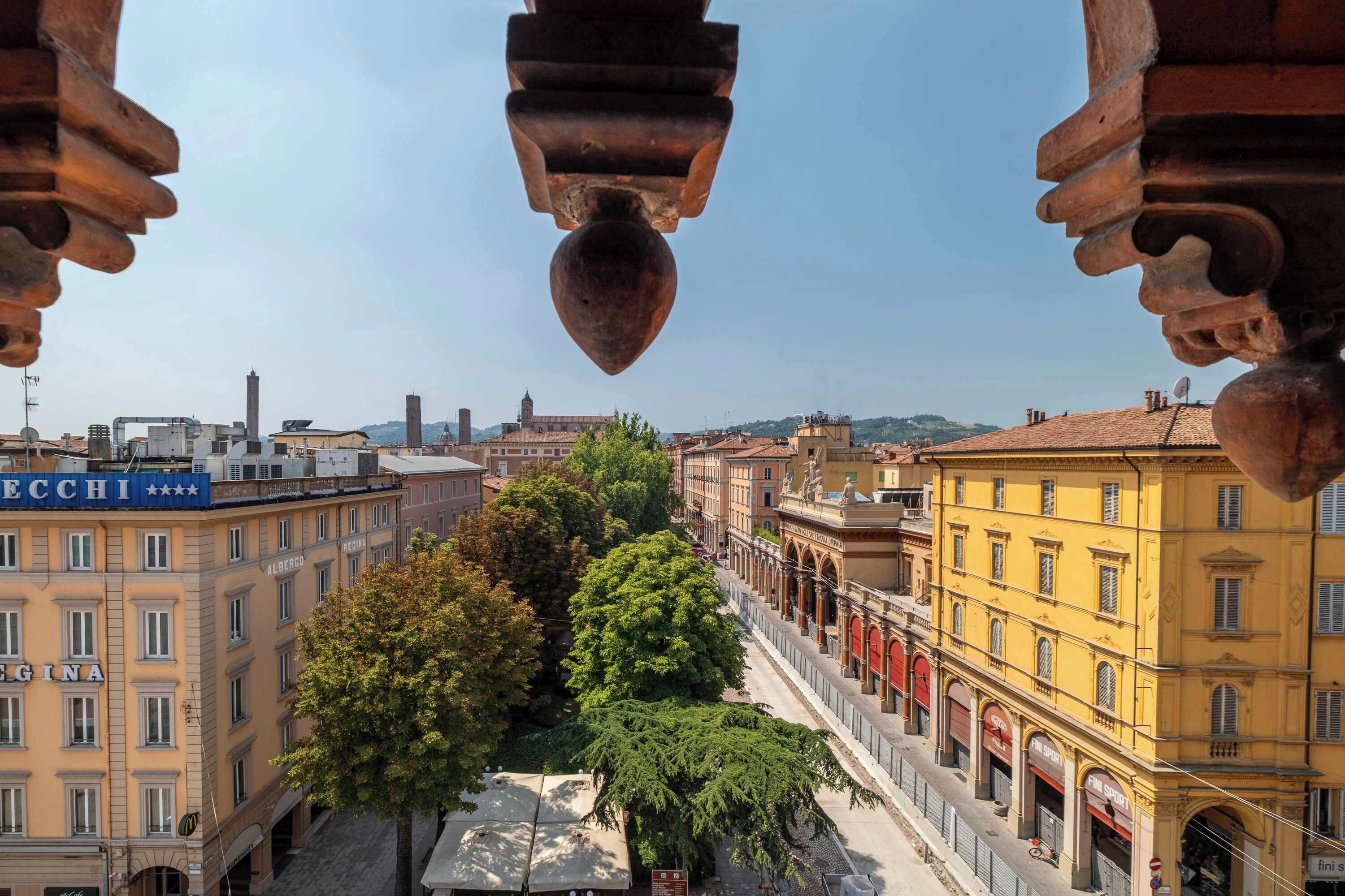 Vista de una calle urbana con edificios, árboles y cielo despejado.
