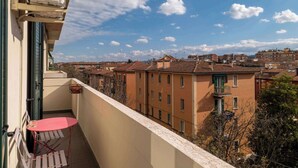 A balcony with a red table and chairs, an air conditioning unit, and a view of a residential area with buildings under a partly cloudy sky. - Casa Marion Stile e Comfort in un Elegante Dimora Bolognese (Bologna)