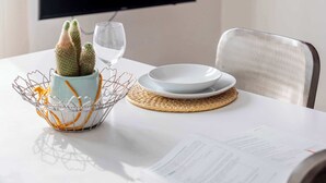 A dining table with a cactus in a wire basket, a glass of water, and a plate with a bowl. Papers are on the table. - Casa Marion Stile e Comfort in un Elegante Dimora Bolognese (Bologna)