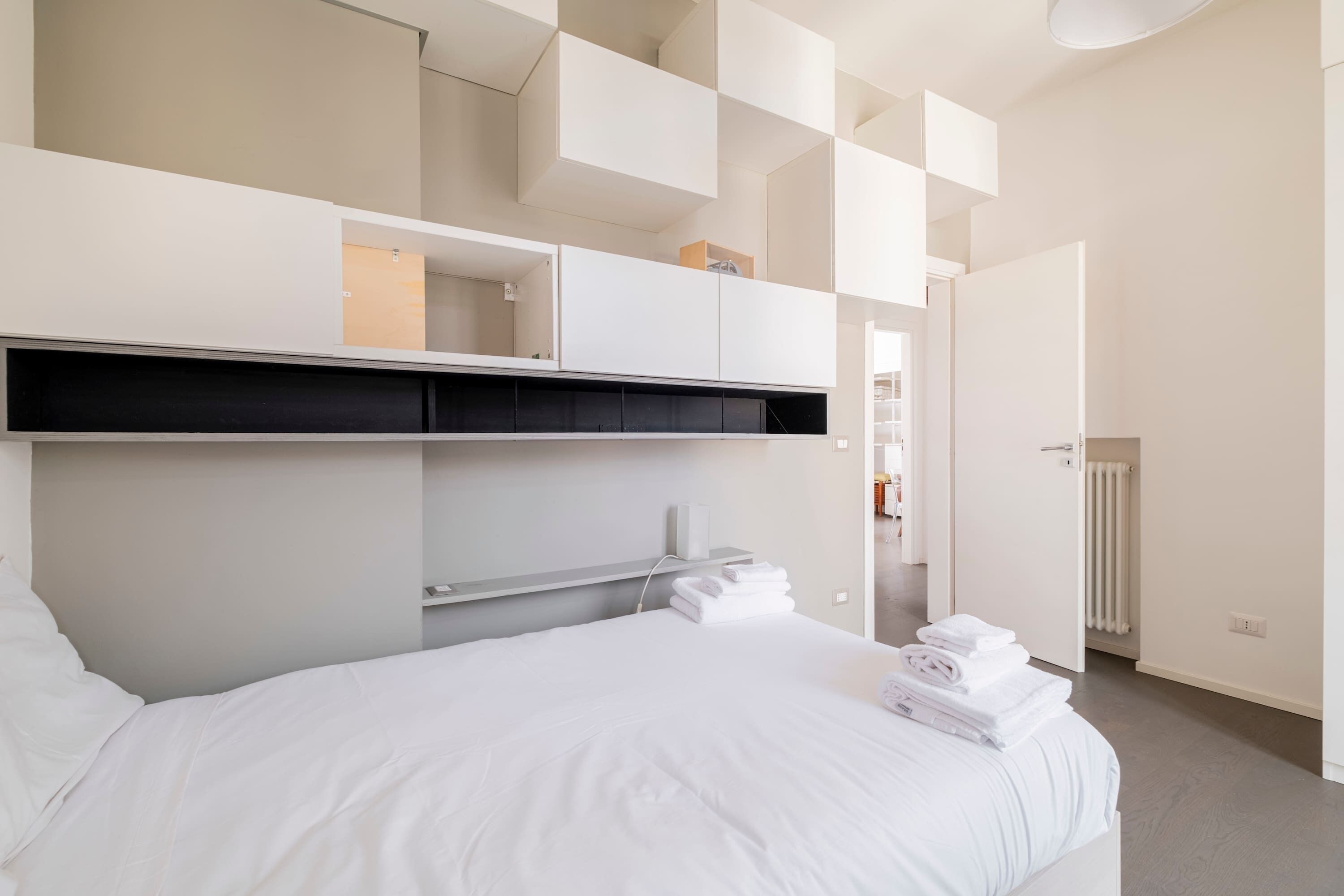 A modern hotel room with a neatly made bed, built-in storage cabinets, and a view of the hallway.