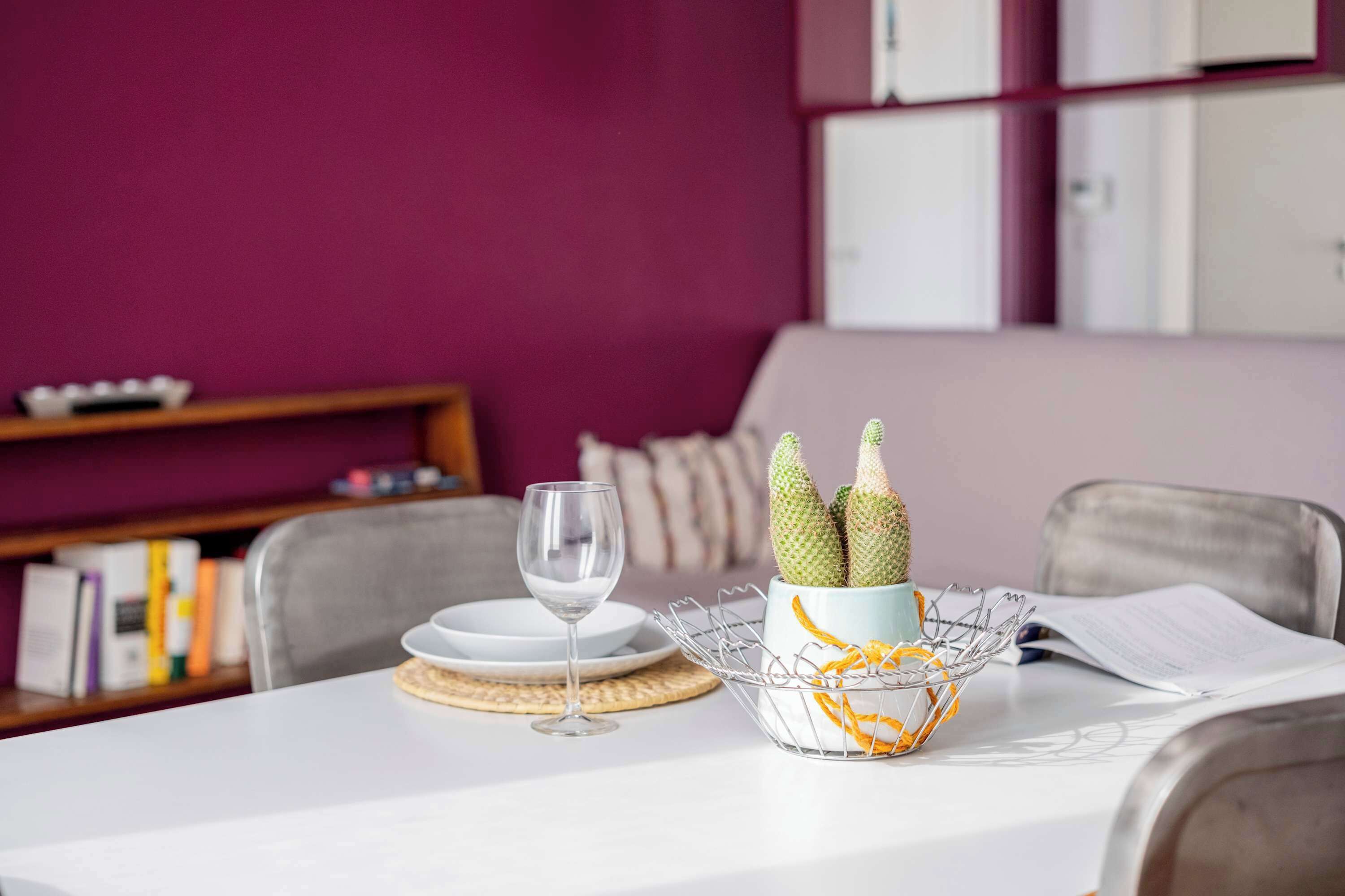 A dining table with a white tablecloth, a wine glass, a basket with a cactus, and a book.