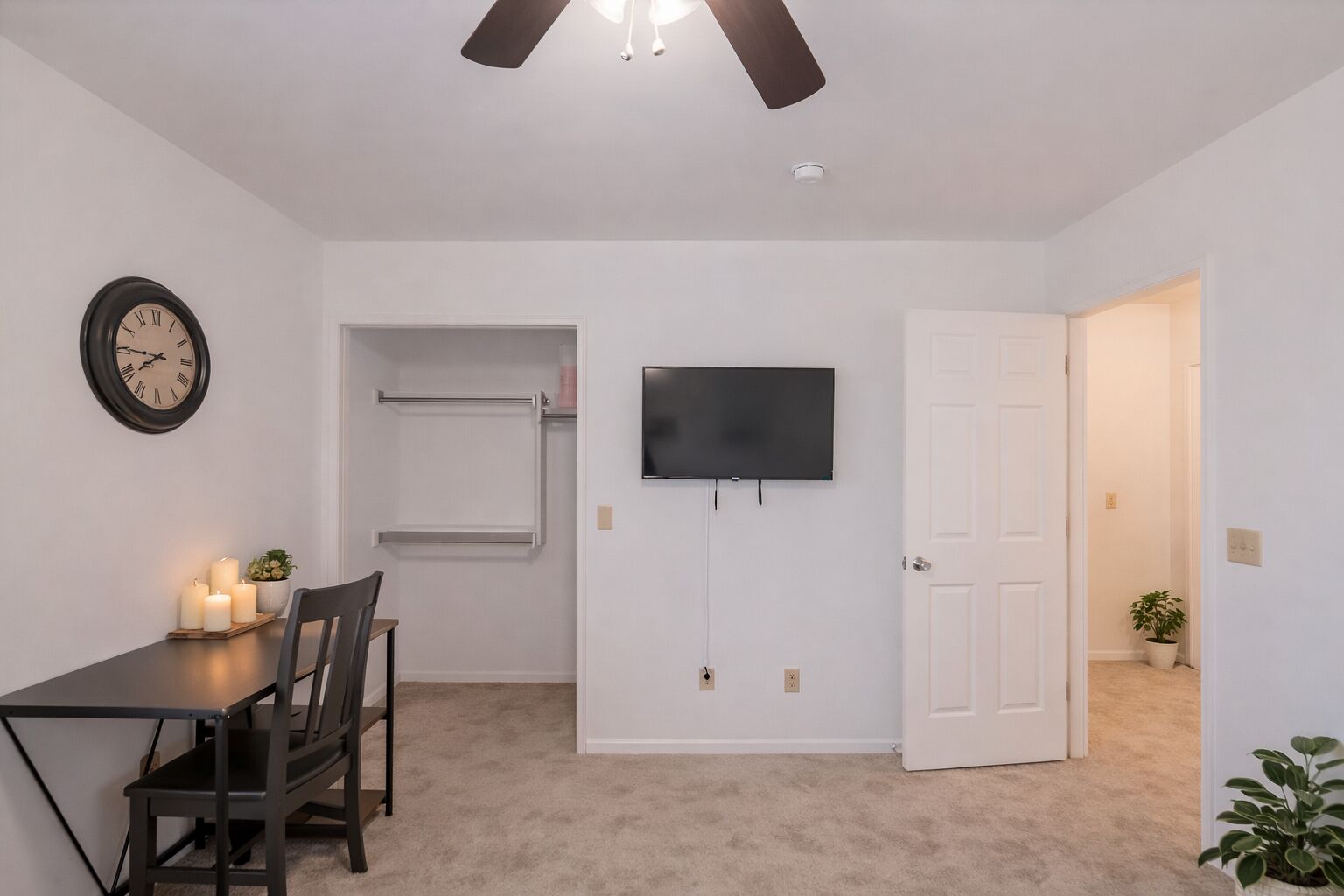 A room with a dining table, chairs, a clock, a television, and a door.