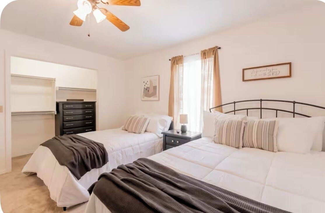 A bedroom with two beds, a ceiling fan, a dresser, and a window with curtains.