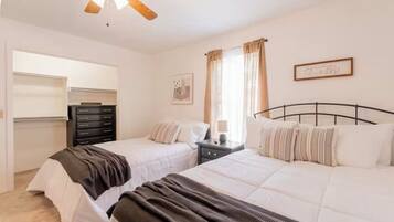 A bedroom with two beds, a ceiling fan, a dresser, and a window with curtains.
