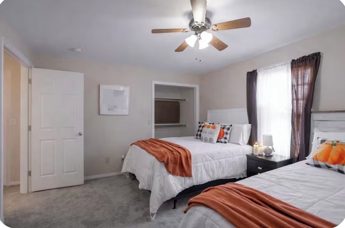 A bedroom with two beds, a ceiling fan, a white door, and a window with curtains.