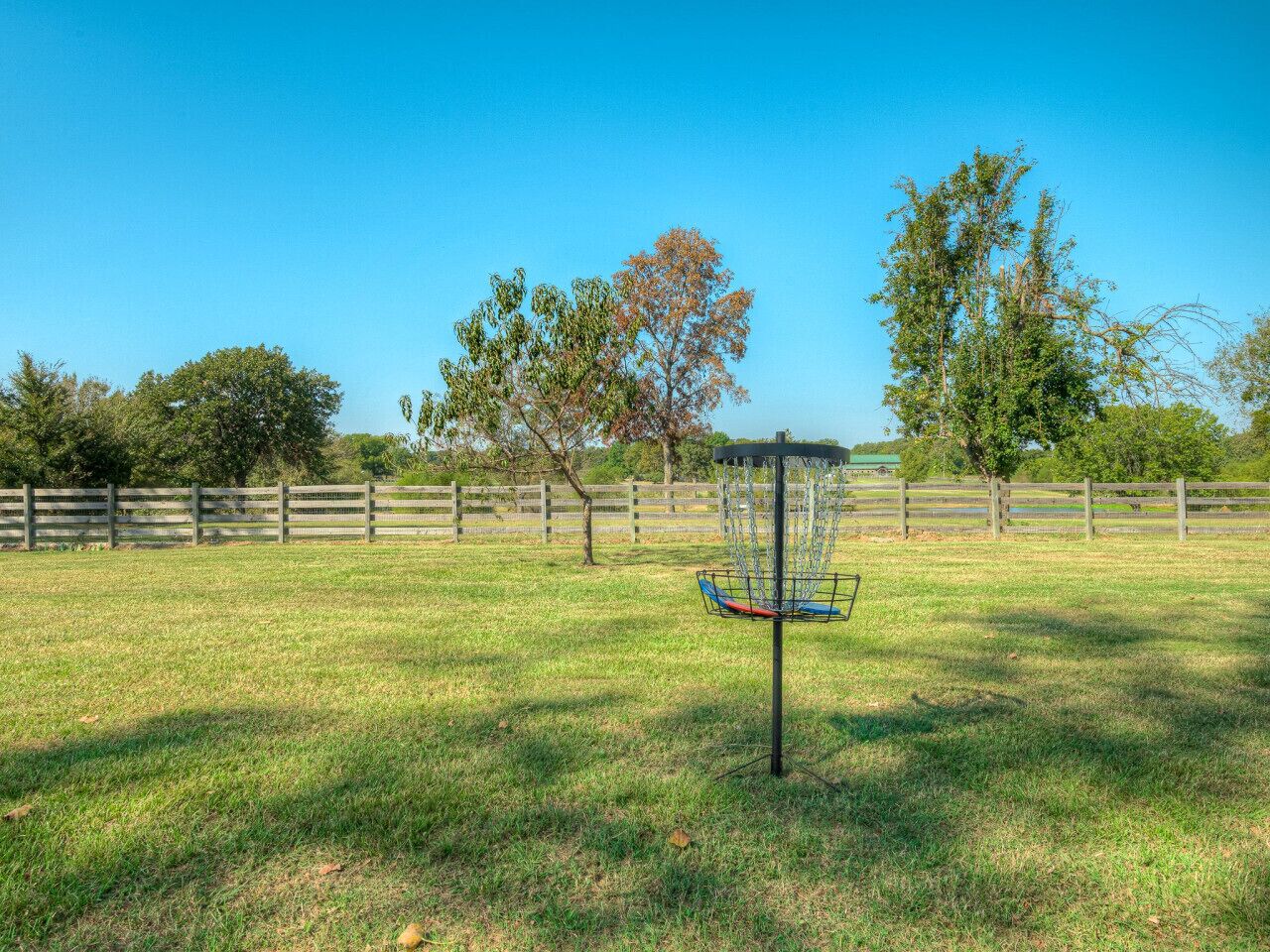 A disc golf basket in a grassy field with a wooden fence in the background.
