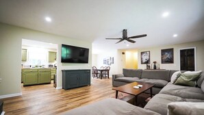A living room with a sofa, coffee table, and a TV mounted on the wall. There is a dining area with a table and chairs in the background. - An explorer's escape - 3 bed 2 bath house with AC in Hico (Hico)