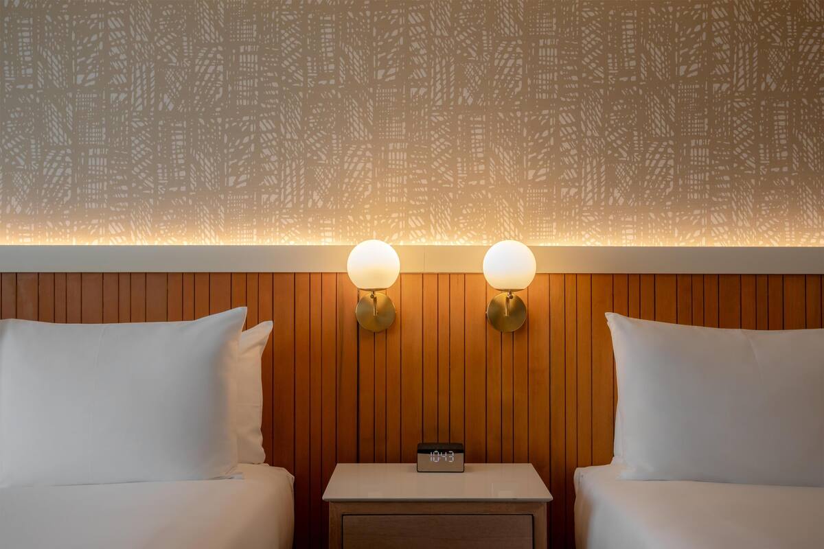 Habitación de hotel con dos camas, un panel de pared de madera y dos lámparas fijadas a la pared.