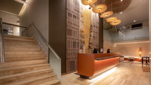 Een moderne hotel lobby met een receptiebalie, een trap en een hoog plafond met hangende lampen.