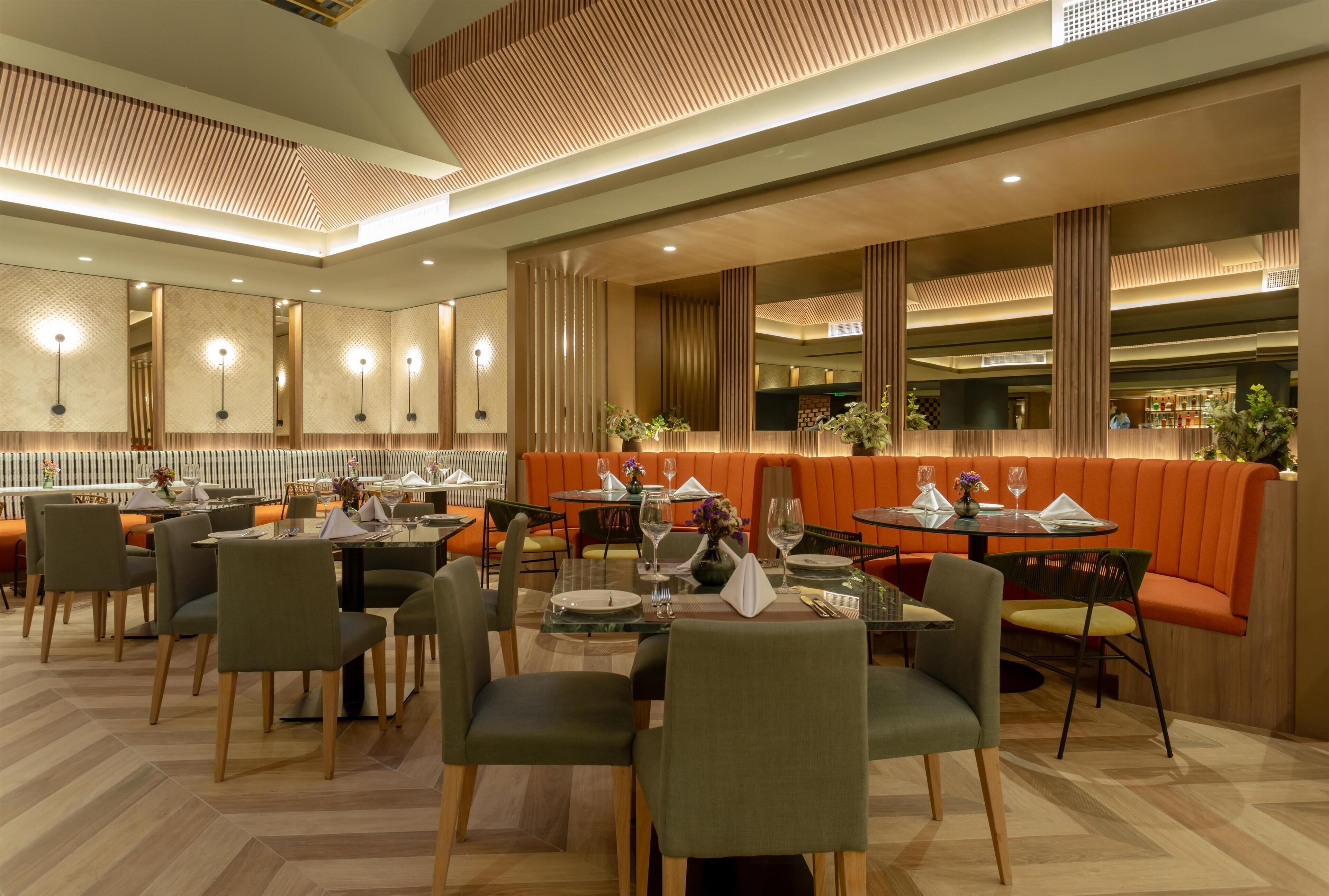 A modern restaurant with multiple dining tables and booths, featuring a wooden ceiling and ambient lighting.