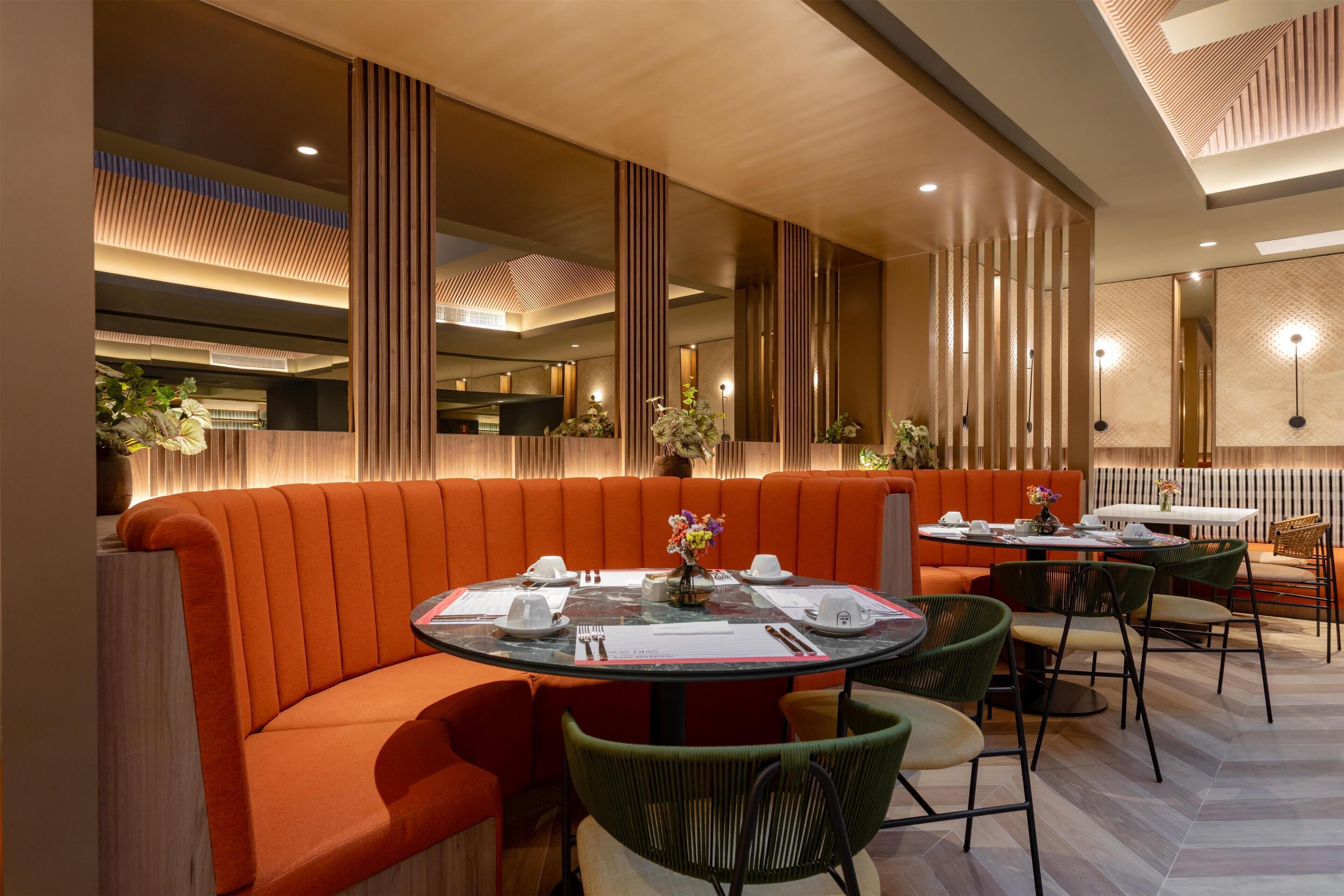 A modern restaurant with a curved orange seating area, a round table with chairs, and a decorative vase with flowers.