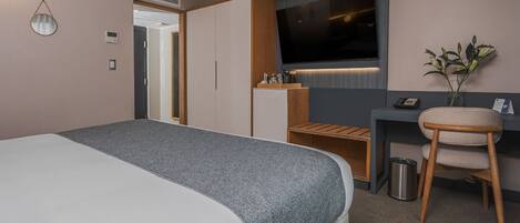 Een hotelkamer met een groot bed, een bureau met stoel, een televisie en een plant.