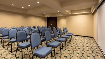 Un salón de conferencias con filas de sillas azules, una alfombra estampada y una puerta al fondo.