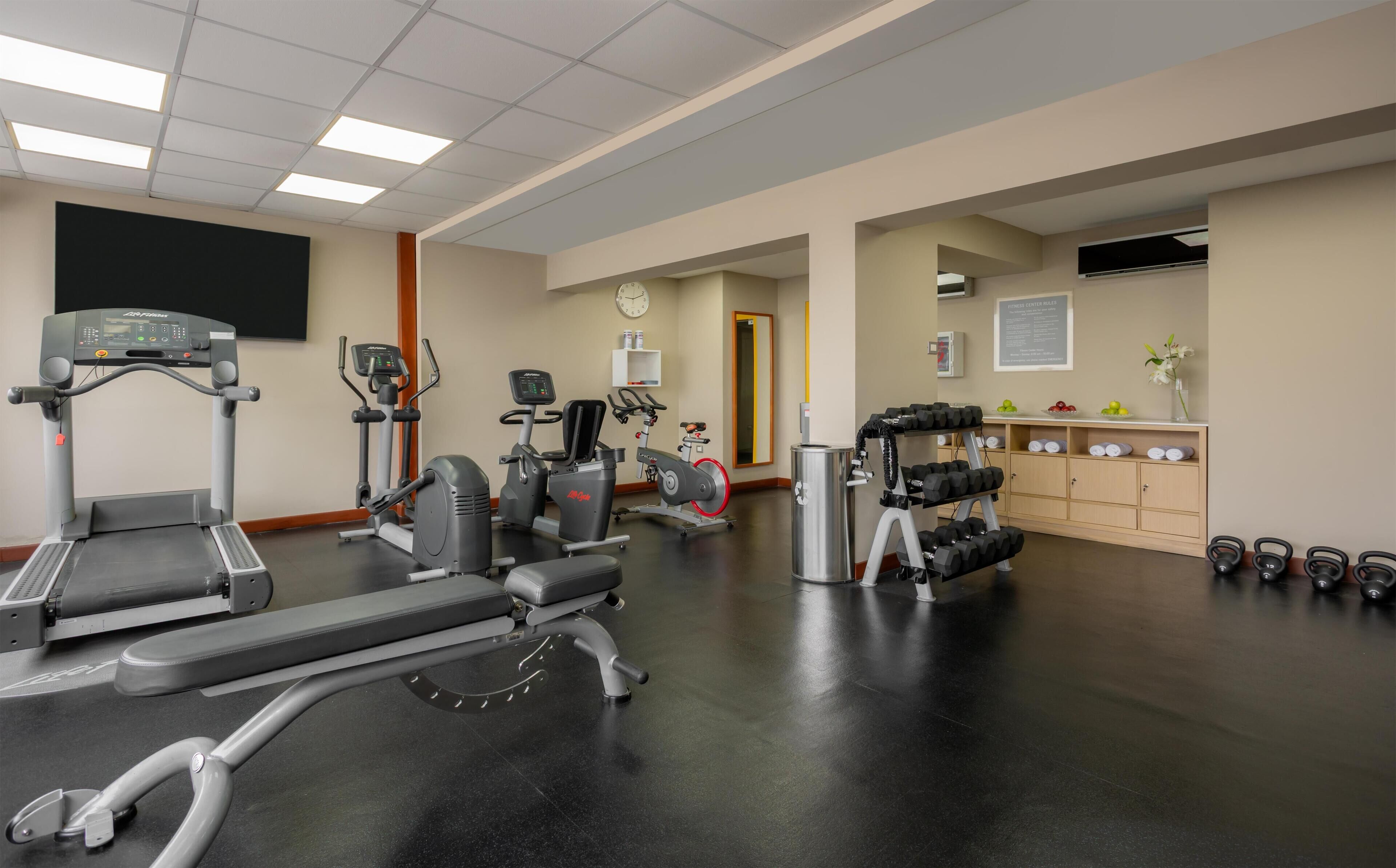 A gym with cardio machines, weightlifting equipment, and a wall-mounted TV.