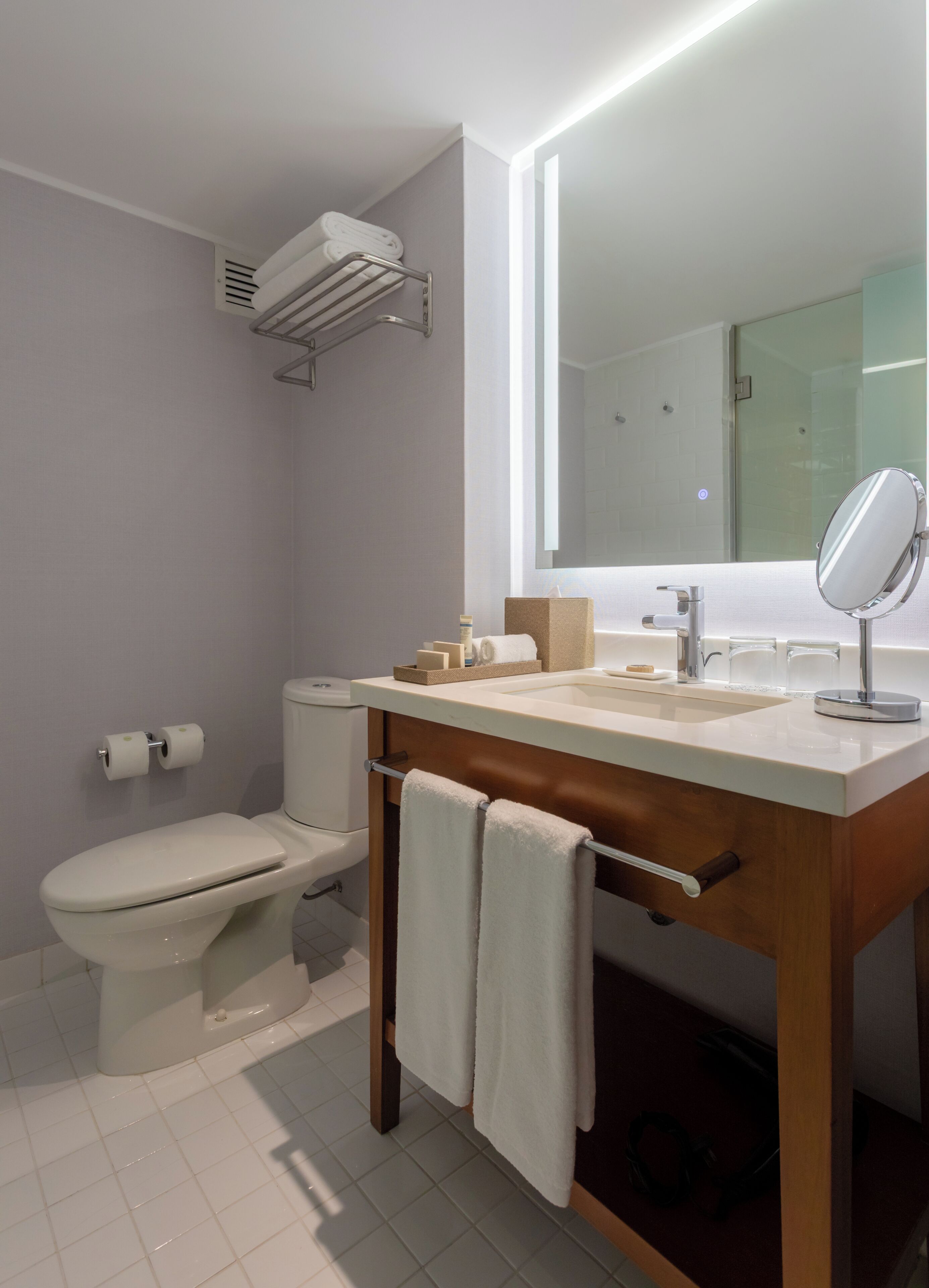 A modern bathroom with a toilet, sink, mirror, towel rack, and a towel hanging on the rack.