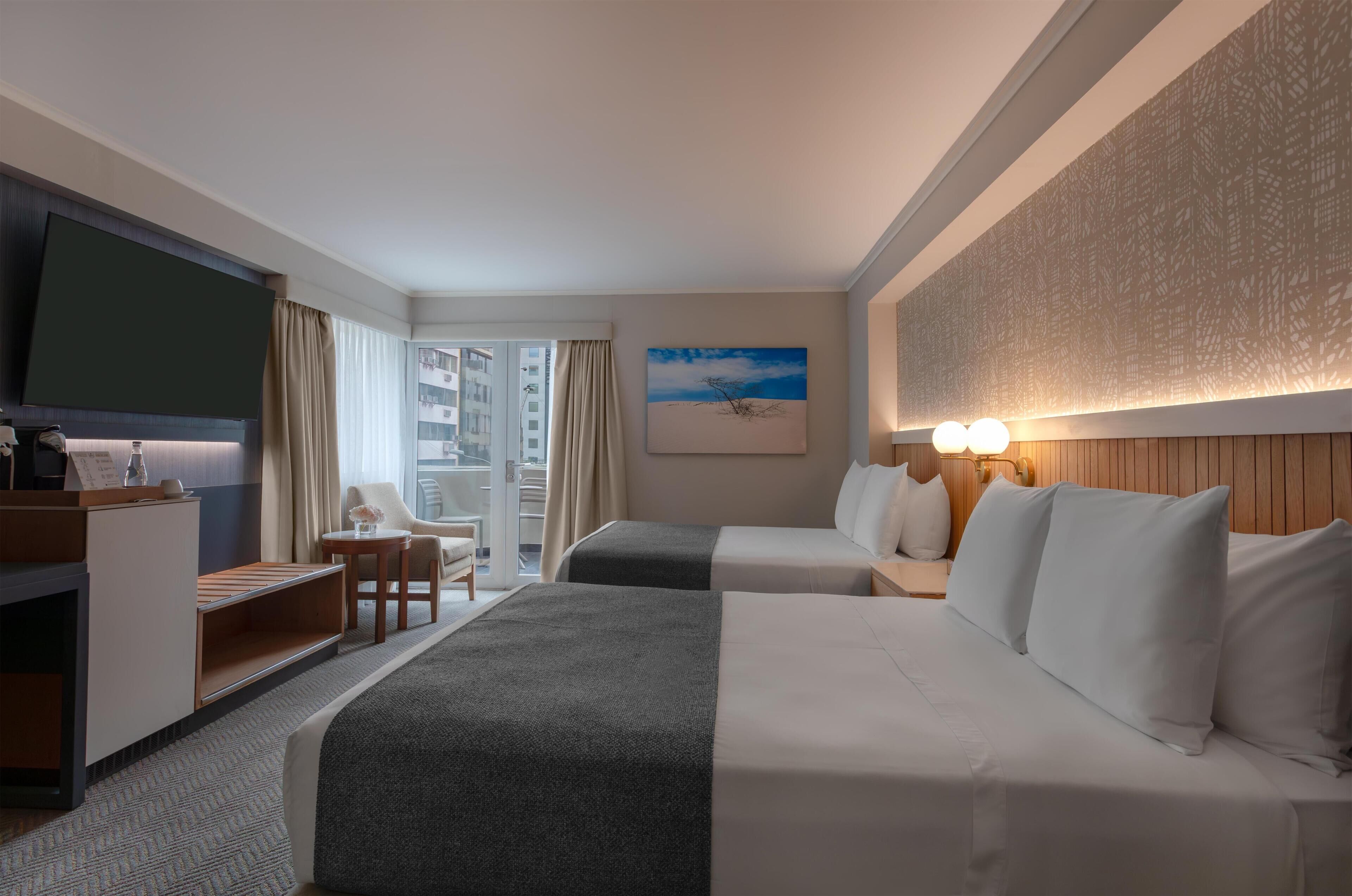 Une chambre d’hôtel avec un lit, un bureau, une chaise, une télévision et une fenêtre avec des rideaux.