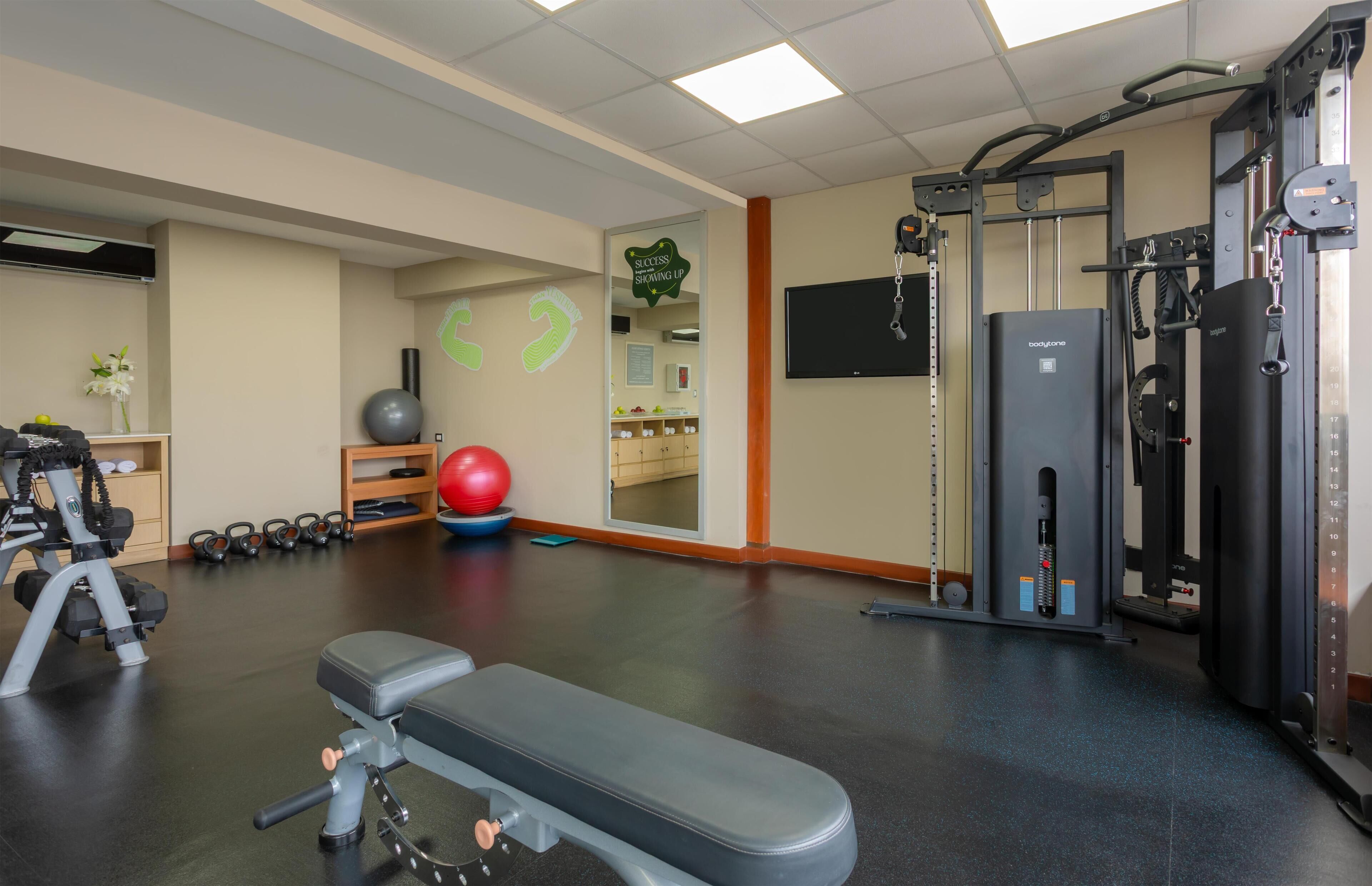 Een sportschool met trainingsapparatuur, een bank en een spiegel.