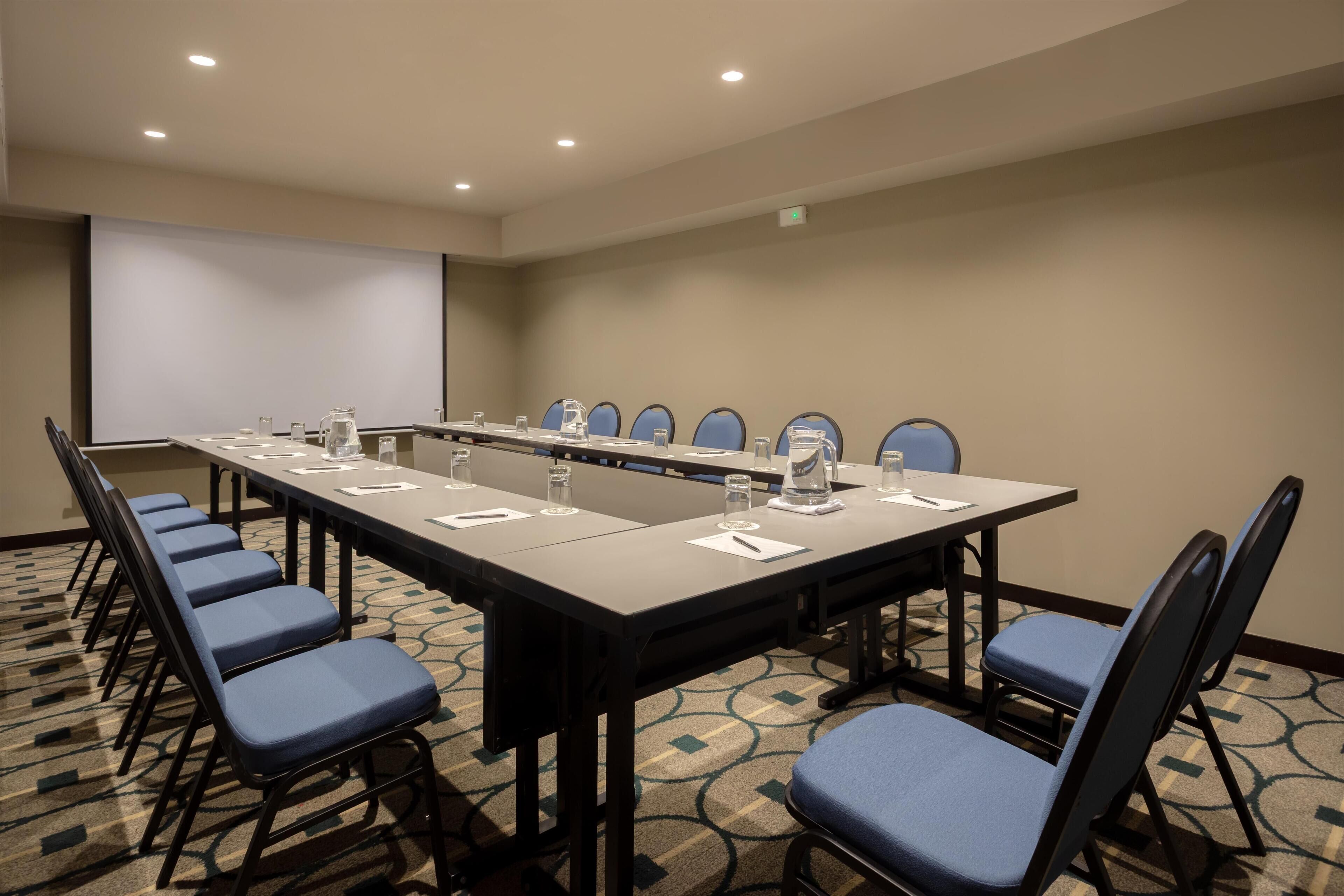 A conference room with a long table, blue chairs, and a projector screen.