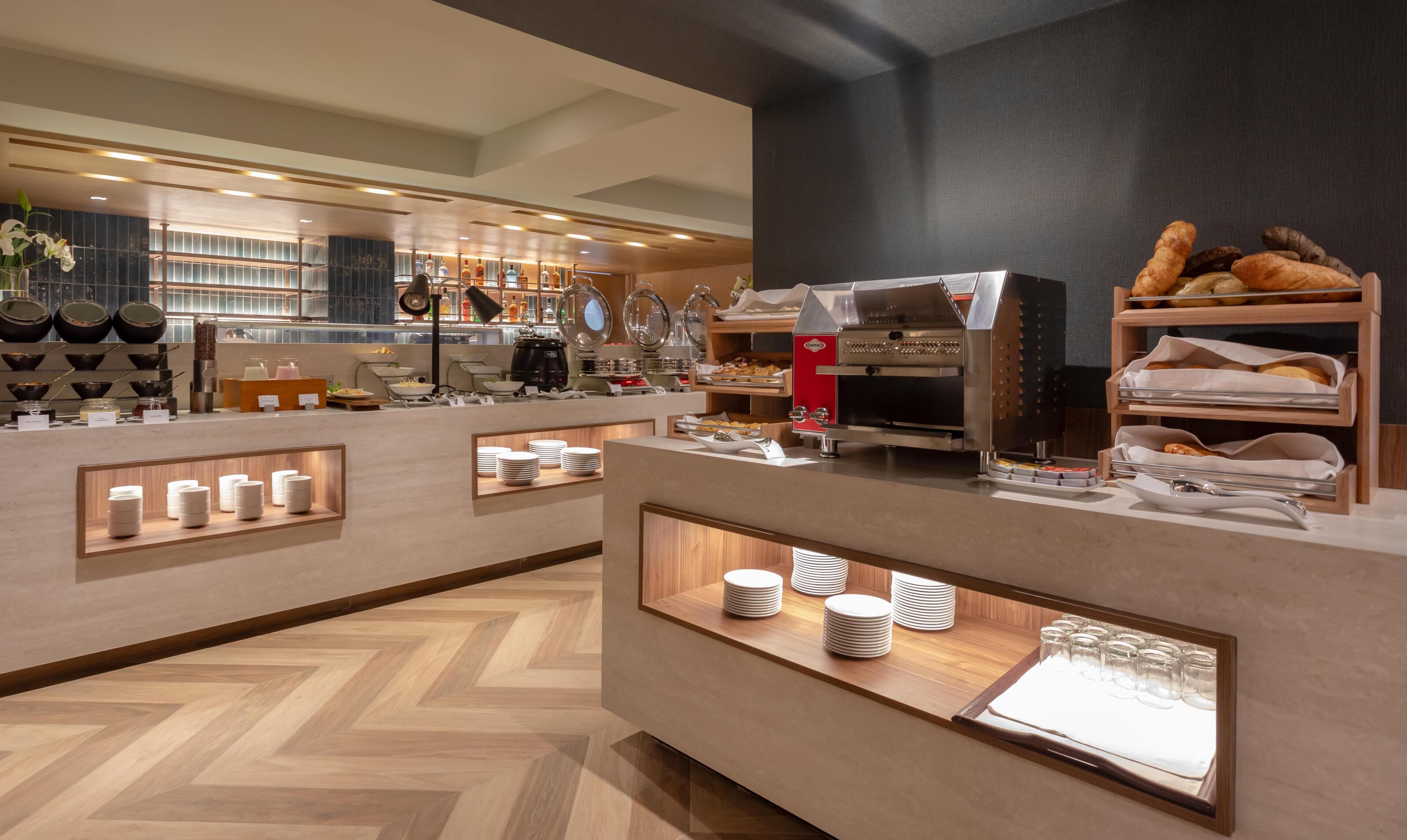 A modern breakfast bar with a coffee machine, pastries, and neatly arranged plates and cups.