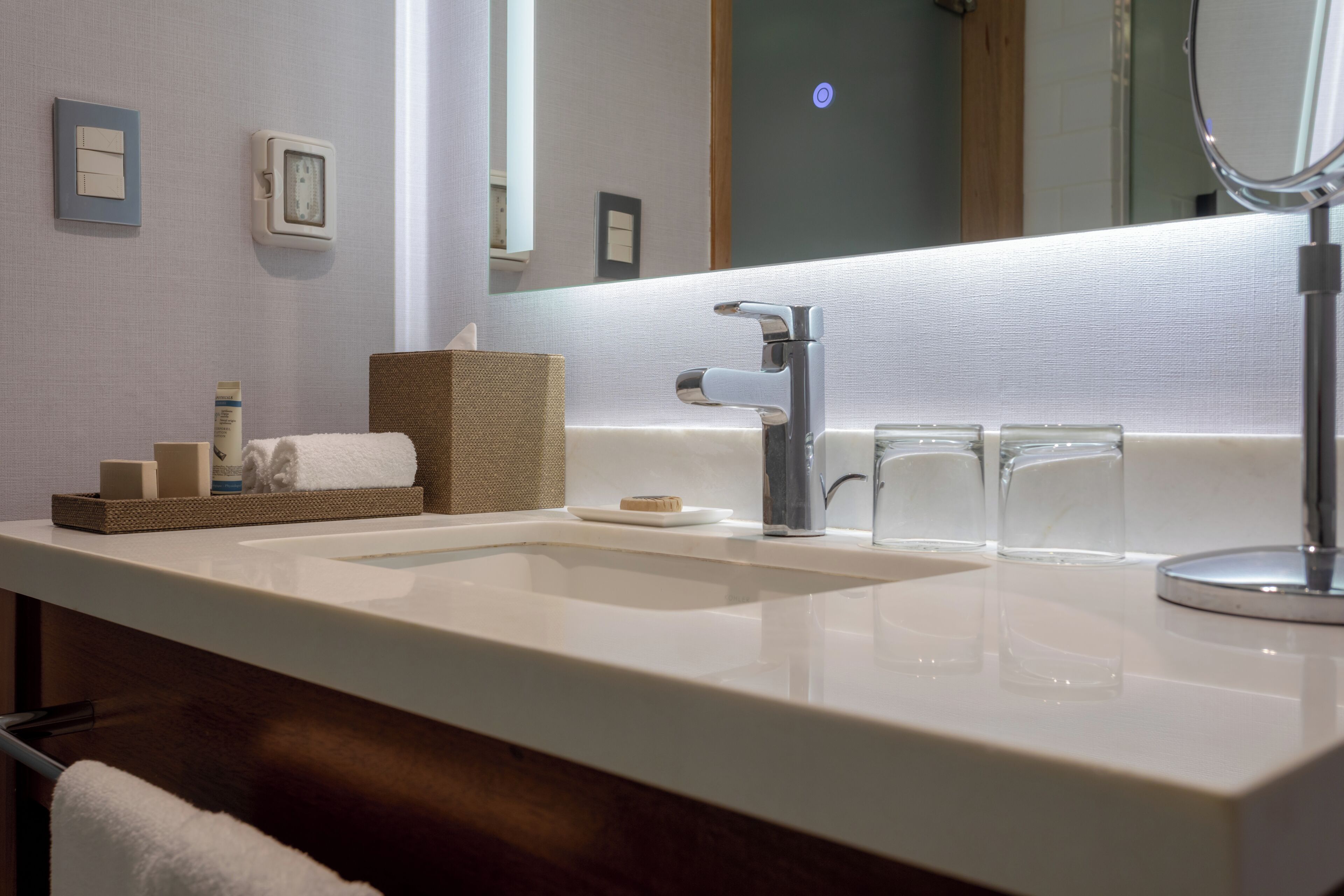 Un bagno con lavandino bianco, specchio, porta asciugamani e saponiera.