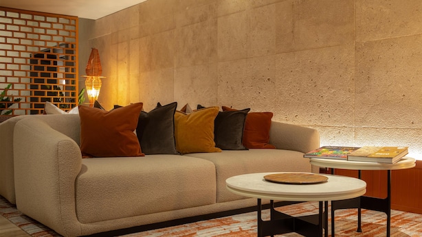 Een moderne woonkamer met een beige bank, een ronde salontafel en een kamerbreed tapijt met patroon.