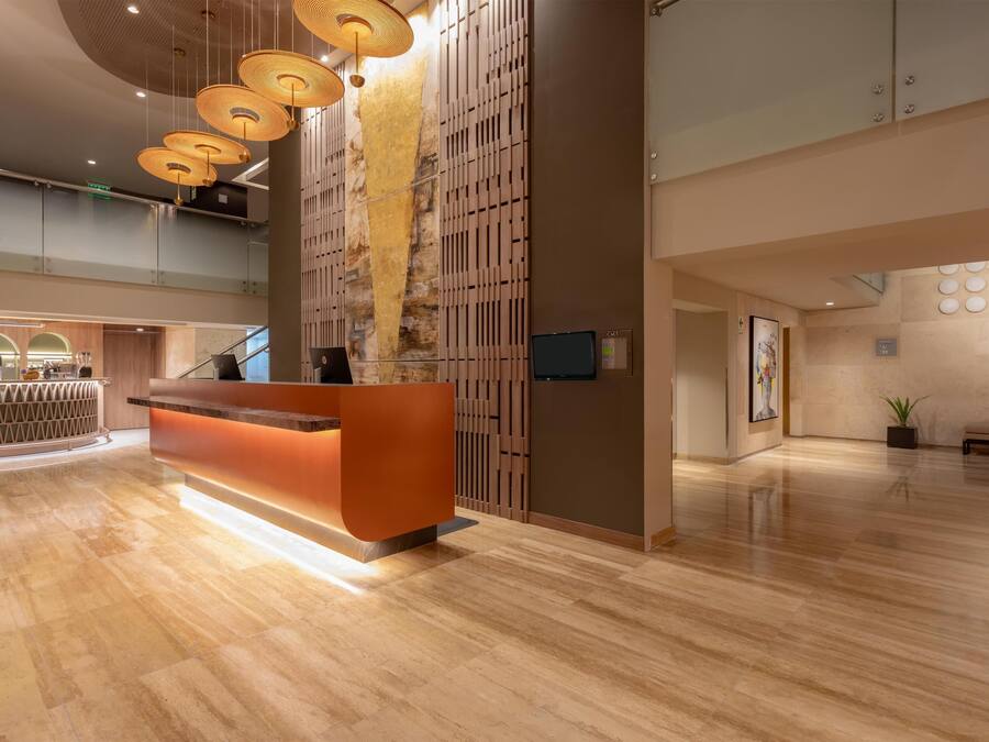 A modern reception area with a wooden reception desk, a staircase, and a large wall with a vertical garden.