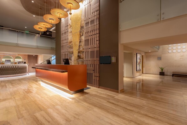 A modern reception area with a wooden reception desk, a staircase, and a large wall with a vertical garden. - Sonesta Hotel Miraflores (Lima)