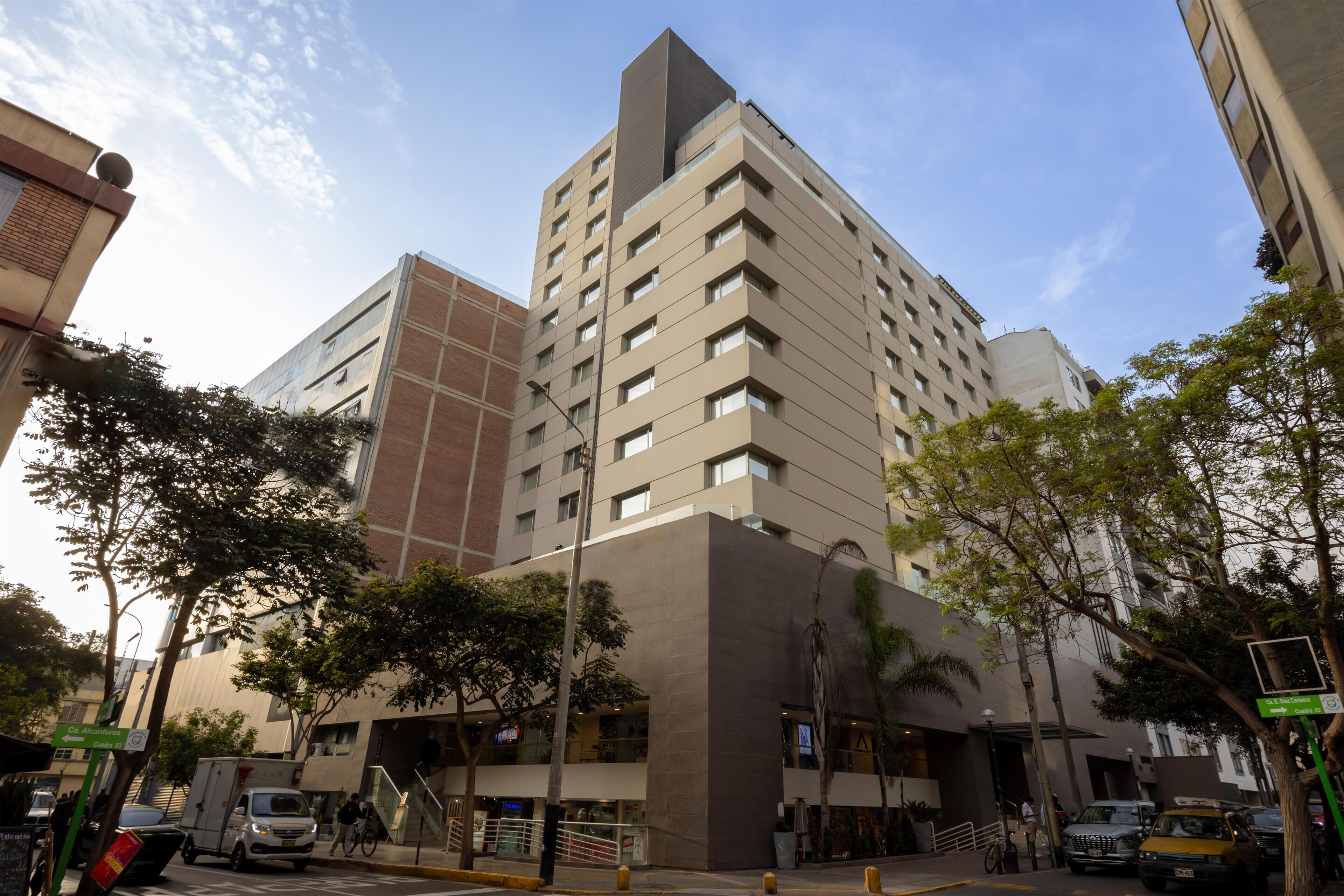 Un immeuble moderne de grande hauteur, doté de nombreux étages, d’une architecture remarquable au niveau des angles et d’une entrée bien visible avec un escalier.